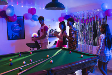 Teenagers enjoying birthday party with pool table and colorful decorations indoors. Celebration,...