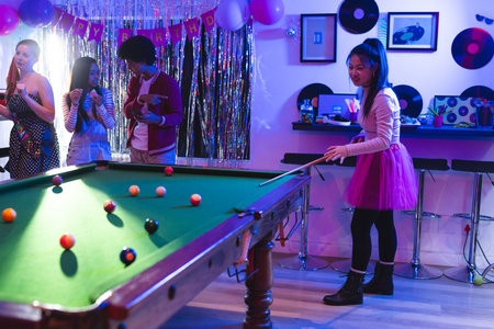 Teen playing pool at birthday party, friends enjoying music and snacks nearby. Billiards,...