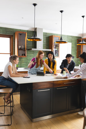 Collaborating on school project, teen friends using tablet and notes in kitchen. Collaboration,...