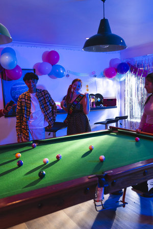 Teenagers enjoying birthday party playing pool in festive decorated room. Celebration, youth,...
