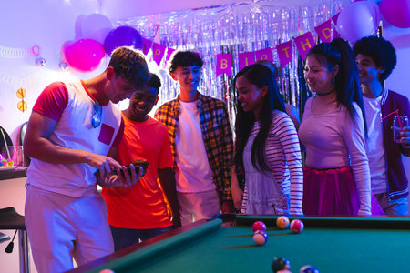 Teenagers enjoying birthday party around pool table, sharing laughs and excitement. Celebration,...