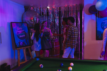 Teenagers celebrating at birthday party with pool table and disco ball decorations. Celebration,...