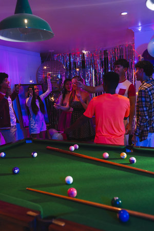 Celebrating around pool table, teenagers with drinks in festive party atmosphere. celebration,...