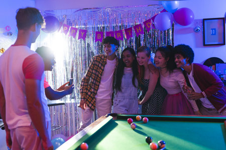 Teen friends posing for group photo at birthday party near pool table. Celebration, friendship, teenagers, fun, leisure, socializingの写真素材
