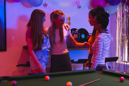 Teen girls celebrating together around pool table, enjoying festive party atmosphere. Celebration,...