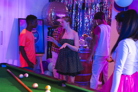 Teenagers enjoying lively party with pool table and disco ball decorations. celebration, youth,...