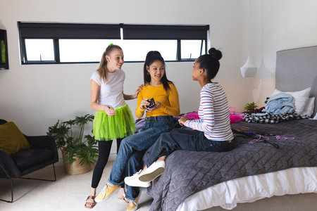 Teen girls laughing and chatting while planning outfits in cozy bedroom. Friendship, bonding, lifestyle, adolescence, leisure, fashionの写真素材