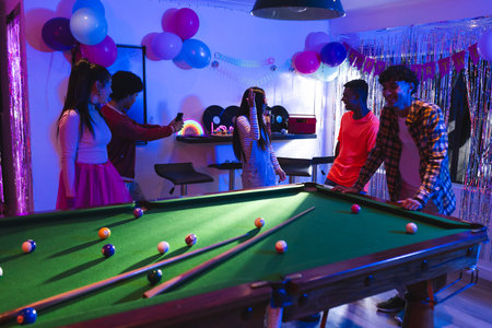 Teenagers celebrating at home, playing pool and taking photos with friends. Party, celebration, friendship, entertainment, leisure, billiardsの写真素材