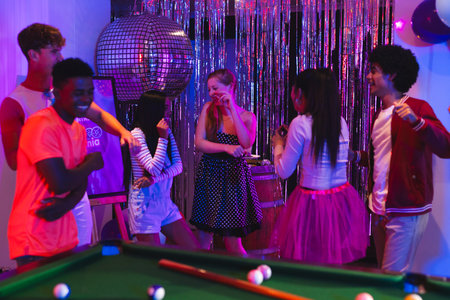 Teenagers dancing and laughing at vibrant party with disco ball and pool table. celebration, music, dance, fun, nightlife, entertainmentの写真素材