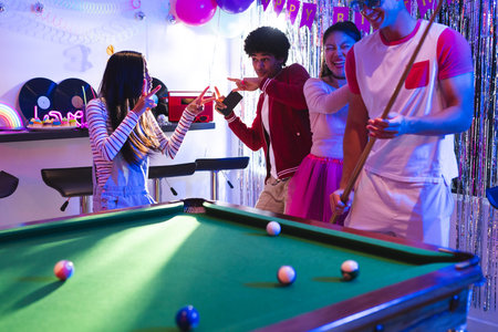 Teens celebrating at home, playing pool and enjoying lively party atmosphere. Teenagers, celebration, billiards, fun, friendship, leisureの写真素材