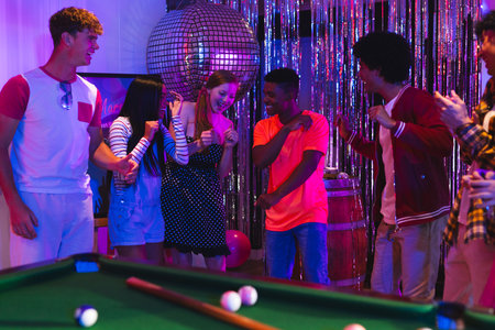 Teens dancing joyfully at party near pool table under disco ball lights. celebration, teenagers, nightlife, entertainment, socializing, leisureの写真素材