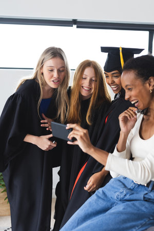Graduates in caps and gowns taking selfie, celebrating success together. Graduation, celebration, achievement, diploma, friends, joyの写真素材