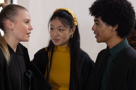 Teens in graduation gowns celebrating together, smiling and chatting happily. celebration, happiness, friends, school, achievement, milestoneの写真素材