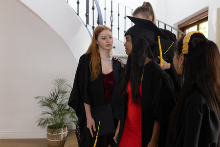 Graduating students in caps and gowns celebrating together at home. Graduation, celebration, achievement, joy, accomplishment, successの写真素材