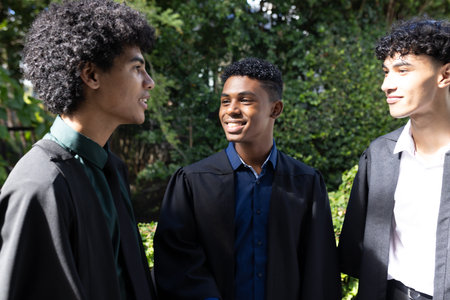 Teen graduates in gowns smiling and chatting outdoors, celebrating achievement. Graduation, accomplishment, ceremony, friendship, education, celebrationの写真素材