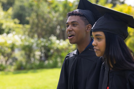 Teen graduates in caps and gowns celebrating success outdoors with smiles. Graduation, celebration,...
