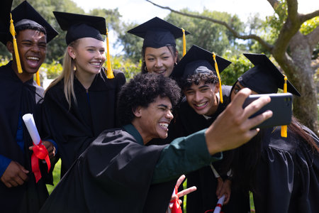Graduating students taking selfie outdoors, celebrating with joy and excitement. Graduation, celebration, achievement, happiness, education, academicの写真素材
