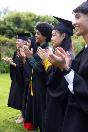 Graduating students in caps and gowns clapping joyfully at outdoor ceremony. Graduation, celebration, academic, success, achievement, commencementの写真素材