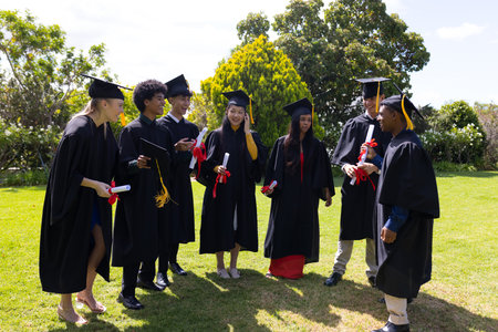 Graduates celebrating together outdoors, holding diplomas and wearing caps and gowns. Graduation, achievement, ceremony, accomplishment, education, traditionの写真素材