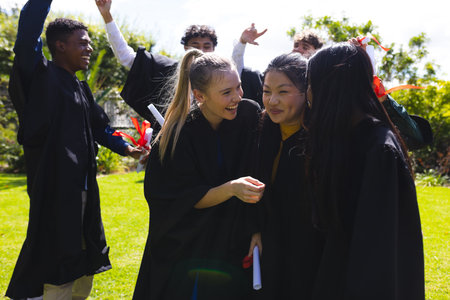 Graduating students celebrating outdoors, smiling and holding diplomas in excitement. Graduation, celebration, achievement, success, education, collegeの写真素材