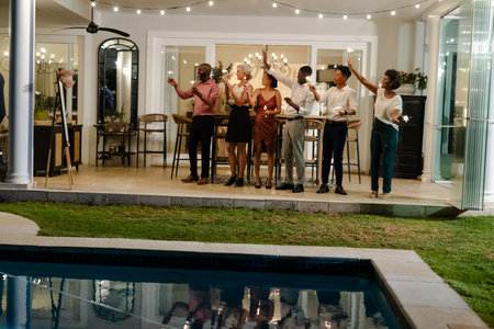 Friends celebrating with sparklers by poolside at evening wedding reception. Celebration, party, festive, joyfulの写真素材