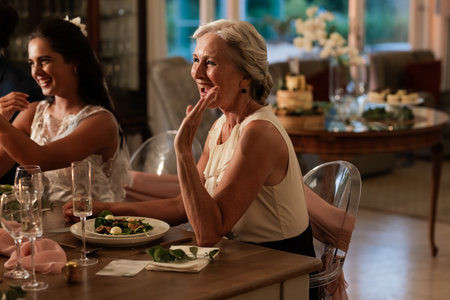 Elderly woman joyfully toasting at wedding reception, enjoying dinner with family. Celebration, happinessの写真素材