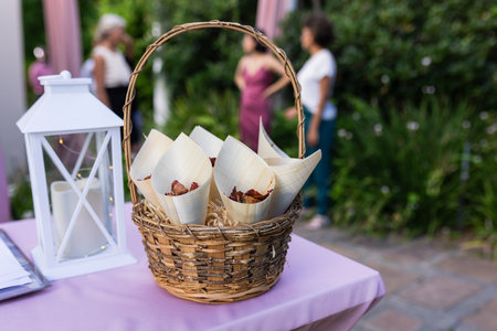 At outdoor wedding, basket of snacks on table with guests mingling nearby. Celebration, reception, marriage, party, catering, refreshmentsの写真素材