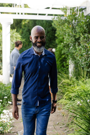 Smiling African American man walking through garden at wedding celebration. event, happiness, outdoors, joyful, lifestyle, eleganceの写真素材