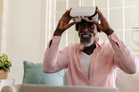 Using VR headset at home, African American man smiling during virtual experience. Technology,...