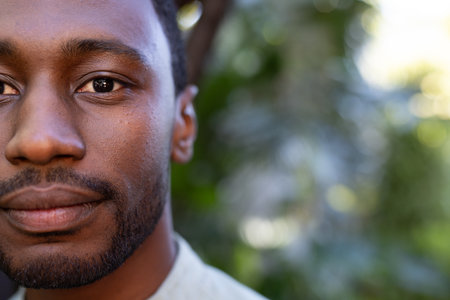 African American man outdoors, looking thoughtful with greenery in background. Contemplation, nature, solitude, tranquility, casual, reflectionの写真素材
