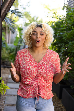 Smiling woman with curly hair talking while walking in garden. Nature, conversation, happiness, communication, stroll, greeneryの写真素材