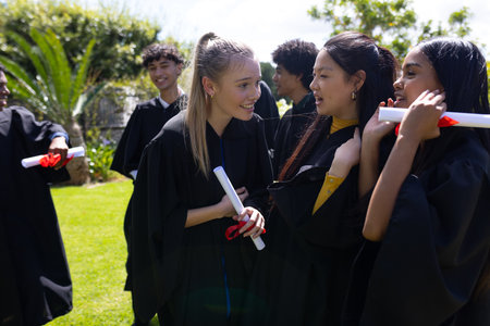 Celebrating outdoors, teens in graduation gowns holding diplomas, smiling joyfully. celebration,...