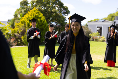 Graduating students celebrating outdoors, Asian girl smiling and receiving diploma. Graduation, celebration, achievement, university, happiness, successの写真素材