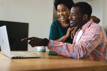 Friends enjoying time together, smiling and pointing at laptop screen at home. Friendship, technology, bonding, casual, discussion, teamworkの写真素材