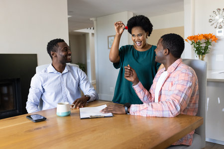 African American friends celebrating new home purchase with keys at dining table. Celebration, friendship, homeownership, happiness, togetherness, joyousの写真素材