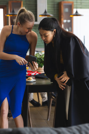 Teen girls in elegant dresses sharing smartphone excitement at celebration event. Friendship, technology, party, connection, lifestyle, fashionの写真素材
