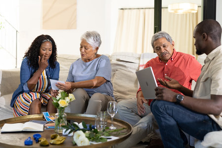 Sharing photos, African American woman with elders and man using tablet at gathering. Family, technology, socializing, togetherness, seniors, digitalの写真素材