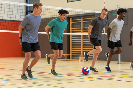 Diverse male volleyball teammates performing knee-raise warm-up drill inside gymnasium by net. Athletes, training, fitness, sports, teamwork, dynamic, professionalの写真素材