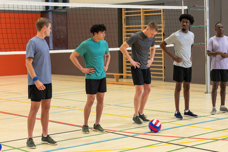 Diverse male volleyball team standing on court with boundary lines, net, volleyball and sneakers. Athletics, teamwork, sport, competition, fitness, activewear, inspirationの写真素材