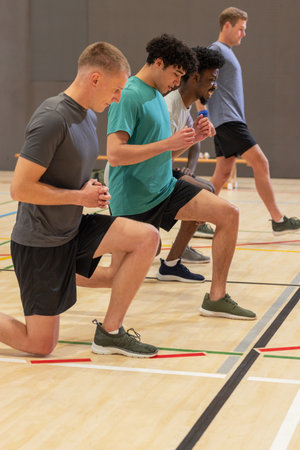 Diverse male workout partners performing lunges in gymnasium in sportswear with dumbbells on bench. Fitness, teamwork, motivation, athletic, training, strength, enduranceの写真素材