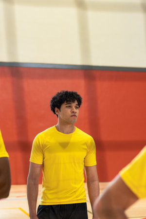 Male teammates practicing in gymnasium wearing yellow shirts and black shorts with red wall padding. Athlete, teamwork, sportsmanship, training, competition, gymnasium, fitnessの写真素材