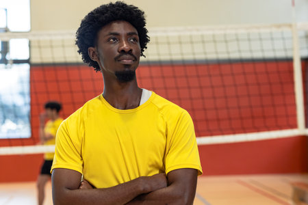 Standing near volleyball net at gym, African American male teammates in yellow jerseys. Athlete, teamwork, sport, competition, dynamic, fitness, trainingの写真素材