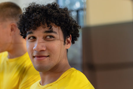 Male teammates standing in sports hall looking right wearing matching yellow athletic shirts....