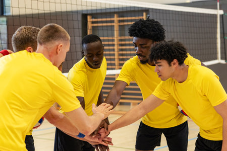 Diverse male volleyball teammates huddling and stacking hands on court with net and boundary lines. Athletes, teamwork, competition, sportswear, dynamic, strength, camaraderieの写真素材