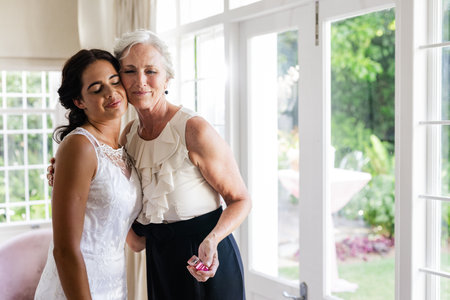 Embracing older woman, bride smiling warmly in sunlit room, celebrating together. Wedding, celebration, family, love, happiness, sunlightの写真素材