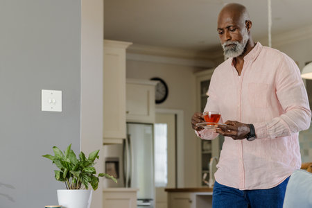 Senior man enjoying cup of tea at home, wearing casual pink shirt. relaxation, leisure, lifestyle, indoors, beverage, comfortableの写真素材