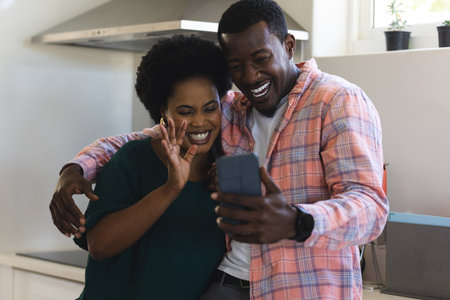 African American couple smiling and video chatting on smartphone in kitchen. Family, happiness, lifestyle, technology, communication, talkingの写真素材