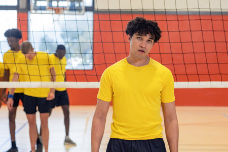 Diverse male volleyball teammates in yellow shirts practicing strategy behind net on polished court. Athletes, teamwork, sport, training, competition, dynamic, determinationの写真素材