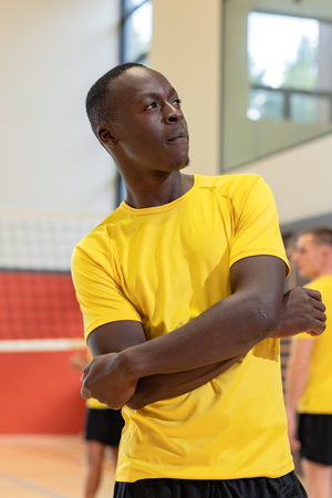 African American male athlete crossing arms by volleyball net in gym wearing yellow jersey shorts. Athletics, team, fitness, competitive, energetic, sport, vigorの写真素材