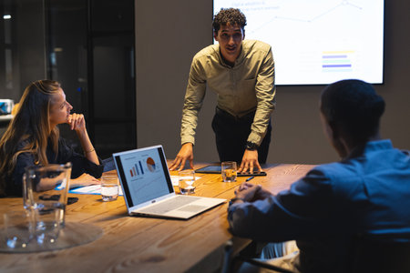 Businessman presenting data to colleagues in conference room during night meeting. presentation,...